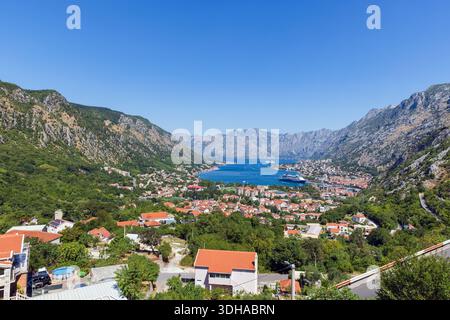 Une vue panoramique sur la ville côtière de Kotor nichée dans une vallée entre des montagnes escarpées. Un port bleu avec des bateaux et des navires, des toits de tuiles rouges, et g luxuriant Banque D'Images