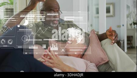 Homme penché en olive-chemise, lunettes pointant femme-rose-top sur canapé, oreiller rose à la maison, regardant AR Banque D'Images