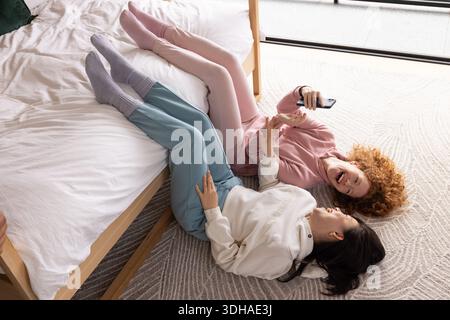 Les vêtements de détente pastel et les chaussettes en tricot reposent sur la moquette à côté du lit en bois, smartphone planant au-dessus Banque D'Images