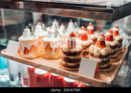Gâteaux festifs de dessert de Noël décorés avec des figures de père noël à la fraise, exposés dans une vitrine de boulangerie avec un éclairage chaleureux et une atmosphère de vacances Banque D'Images