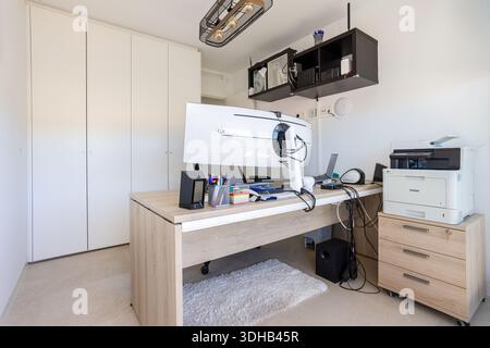 Bureau à domicile bien équipé avec écran incurvé, imprimante, tiroirs de rangement et grand éclairage de l'espace de travail Banque D'Images