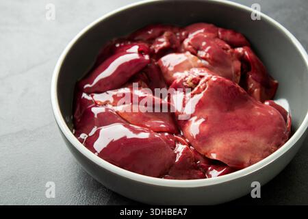 Foie de poulet cru dans un bol gris sur fond de table gris foncé Banque D'Images