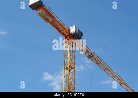 Crochet et bras de grue à tour suspendus haut contre un ciel bleu clair sur un chantier de construction actif Banque D'Images