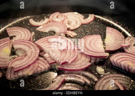 Gros plan de la friture d'oignons rouges frais hachés dans une poêle noire Banque D'Images