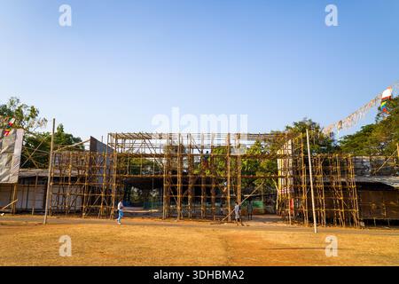 Thrissur, Inde - 12 mars 2023 : deux ouvriers sont vus assembler un échafaudage en bambou pour une grande structure temporaire sur un champ d'herbe sèche, avec des arbres et un ciel dégagé en arrière-plan. Banque D'Images
