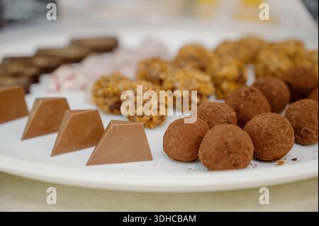 Truffes au chocolat assorties et bonbons faits main sur une assiette blanche pour une table à desserts. Truffes au chocolat en poudre de cacao et chocolat au lait sur un blanc Banque D'Images