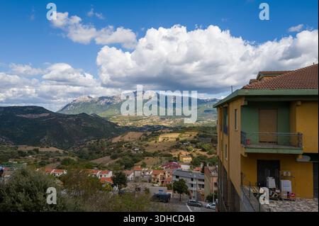 Orgosolo, Italie - 25 septembre 2023 : une vue sur la campagne et les montagnes est vue depuis le bord d'un quartier résidentiel, avec des bâtiments au premier plan et un ciel partiellement nuageux au-dessus. Banque D'Images