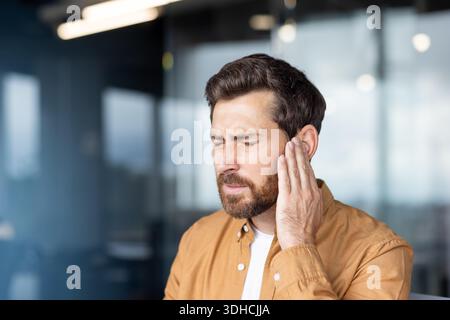 Homme serrant son oreille dans la douleur, montrant des maux d'oreille sévères et l'inconfort de l'infection, acouphènes ou perte auditive stressé, fatigué, et cherchant de l'aide médicale pour le soulager Banque D'Images