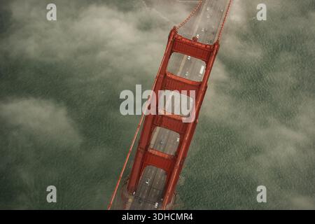 Vue aérienne de l'emblématique Golden Gate Bridge perçant une mer de brouillard, ses tours vermillon contrastant avec les tons sourds de l'eau, San F. Banque D'Images