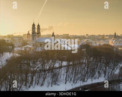 Vue aérienne de l'église de nouveaux Casimir et la lueur dorée du soleil touchant les toits enneigés, Vilnius, comté de Vilnius, Lituanie. Banque D'Images