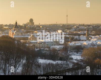 Vue aérienne sur le paysage urbain enneigé, où le dôme de l'église de Casimir brille sous la douce lumière dorée du soleil, la tour de télévision de Vilnius perçant le Banque D'Images