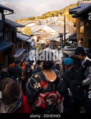 Kyoto, Japon - 18 janvier 2026 : vue d'une scène de rue animée où une femme dans un kimono sombre avec un obi rouge se déplace à travers une foule près de la traditionnelle w Banque D'Images
