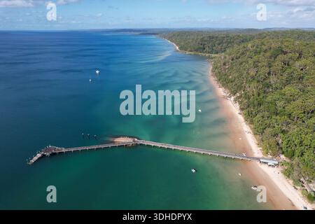 Vue aérienne d'une longue jetée s'étendant dans l'océan turquoise cristallin, contrastant avec la plage de sable et la forêt verdoyante, Eurong, Queensla Banque D'Images
