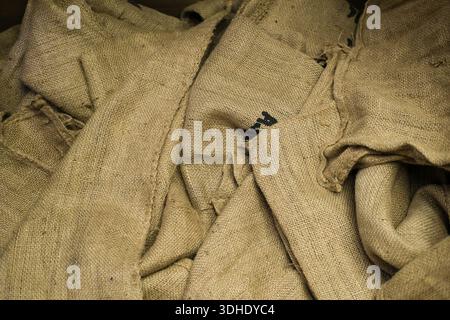 Vue horizontale de sacs de jute avec coutures visibles et fixations de corde ; armure beige grossière, disposition en couches, éclairage artificiel intérieur, modéré Banque D'Images