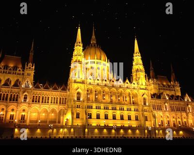 Un bâtiment du Parlement hongrois magnifiquement illuminé la nuit le long du Danube, mettant en valeur l'architecture gothique emblématique de Budapest. Banque D'Images