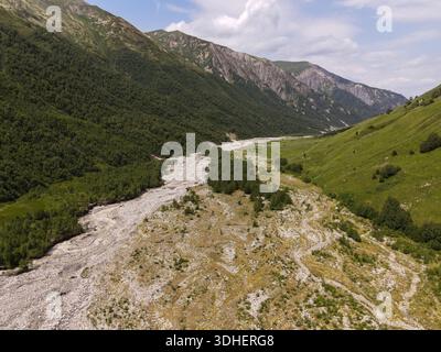 Vue aérienne d'une large vallée alpine dans le Grand Caucase de Géorgie montre un lit de rivière tressé serpentant entre les pentes boisées et les collines herbeuses sous-jacentes Banque D'Images