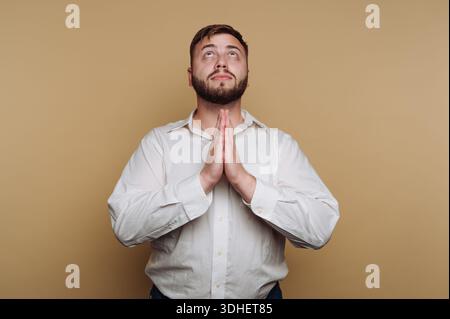 Homme en chemise blanche priant sur fond beige. Banque D'Images