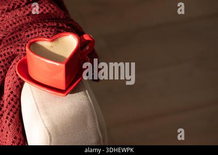 Tasse de café en forme de coeur sur fauteuil avec couverture rouge. Nature morte confortable pour la Saint-Valentin Banque D'Images