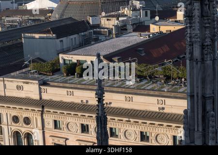Terrasse sur le toit et statue vue du sommet de la cathédrale de Milan, surplombant la façade du bâtiment historique et les toits en dôme de verre au coucher du soleil. Banque D'Images