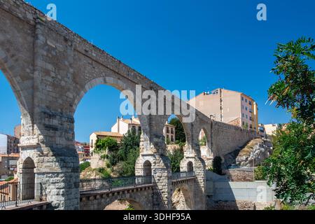 Aqueduc historique de Teruel, en Espagne, avec de grandes arches en pierre et une passerelle piétonne, entouré de bâtiments urbains et d'une végétation estivale sèche. Banque D'Images
