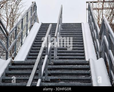 Large escalier extérieur en acier enneigé avec rampes pour vélos des deux côtés, vu de dessous sous le ciel couvert d'hiver. Banque D'Images