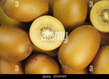 Kiwi doré tranché en gros plan vue de dessus sur de nombreux kiwis jaunes frais et juteux comme fond. Banque D'Images
