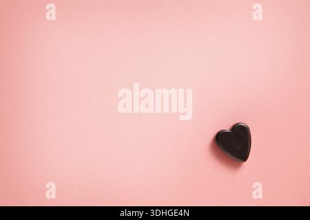 Une composition minimaliste avec un petit coeur noir placé sur un fond rose pastel doux, créant un calme et romantique avec un espace copie. Banque D'Images