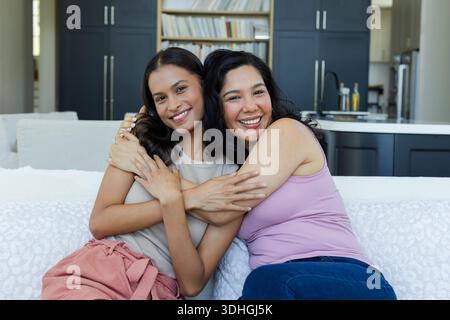 Maman et fille diverses assis sur un canapé léger embrassant et souriant dans le salon décloisonné Banque D'Images