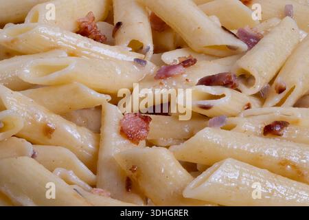 Pâtes penne instantanées garnies de bacon croustillant et d'huile d'olive, pâtes penne préparées rapidement combinées à de petits morceaux de bacon et à un enrobage d'huile savoureux Banque D'Images