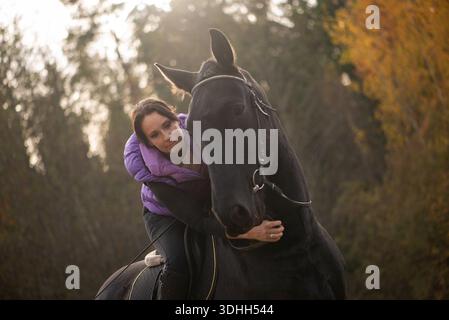 Image verticale capturant une femme d'âge moyen embrassant son cheval noir, baignée de lumière naturelle chaude, symbolisant la confiance, la compagnie et la paix RU Banque D'Images