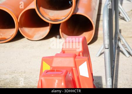 Pile de tuyaux d'égout en plastique derrière des barrières rouges de sécurité routière Banque D'Images