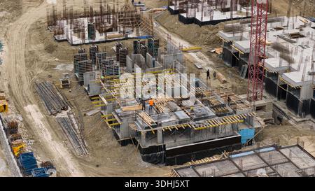 Vue aérienne détaillée des ouvriers de la construction et des coffrages sur un projet de construction résidentielle avec une grue à tour à proximité. Banque D'Images