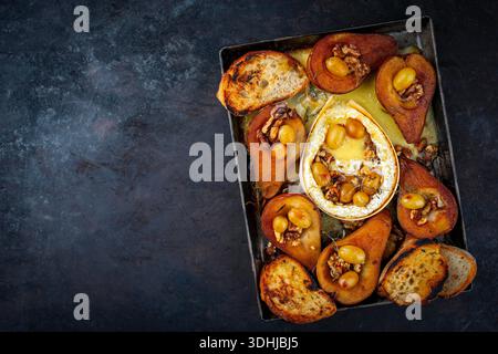camembert cuit au four avec poires glacées caramélisées, noix et raisins et baguette servie sur une assiette en métal rustique Banque D'Images