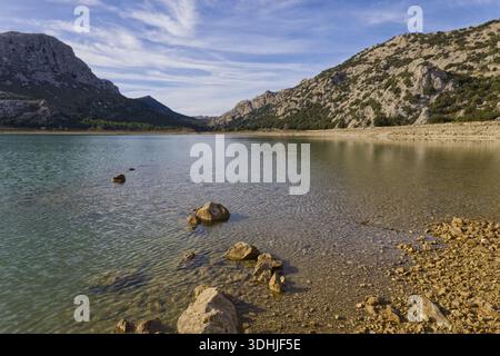 Pierres sur le rivage du réservoir Cúber dans les montagnes de la Serra de Tramuntana, Majorque, sous un ciel bleu avec des nuages. Banque D'Images