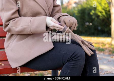 Femme élégante ajustant des gants beiges élégants ornés de clous métalliques, mettant l'accent sur le confort, la mode saisonnière et la chaleur sur une journée d'automne croustillante dans un Banque D'Images