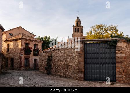 Rue du village de Medinaceli avec des maisons traditionnelles en pierre, un grand mur de pierre, une porte métallique et un clocher baroque Banque D'Images