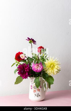 Un vase contient une variété de fleurs fraîches avec différentes couleurs. Les fleurs sont placées sur une table rose. Derrière le vase se trouve un mur Uni dans un roo lumineux Banque D'Images