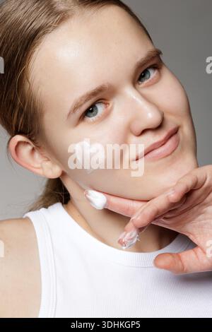 Gros plan portrait studio de jeune femme avec la crème visage en forme de coeur sur la joue. Idéal pour la bannière de site Web de soins de la peau ou l'annonce sociale sur la routine hydratante Banque D'Images