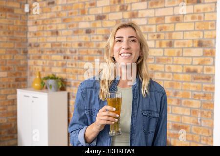 Femme mi-adulte portant une veste en denim tenant le verre de bière contre le mur de briques par armoire, vase Banque D'Images