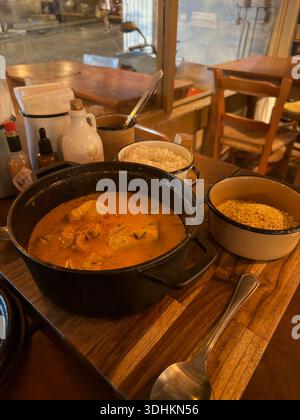 Ragoût de fruits de mer traditionnel servi dans une casserole avec du riz et des accompagnements sur une table de restaurant en bois, lumière intérieure chaude. Banque D'Images