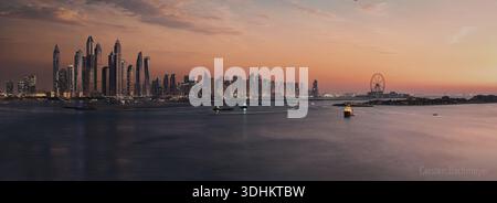Un panorama époustouflant sur les gratte-ciel de Dubaï au coucher du soleil, avec le soleil plongeant sous l'horizon, projetant des teintes chaudes à travers le ciel et se reflétant sur le cal Banque D'Images