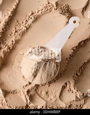 poudre végétalienne aromatisée au chocolat whey protein dans une cuillère sur fond de poudre, vue de dessus Banque D'Images