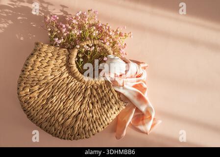 Sac à main en paille tissée avec écharpe soyeuse et fleurs. Élégant été Fashion Flatlay sur fond de pêche Banque D'Images