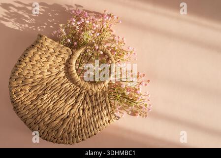 Sac à main en paille tissée avec des fleurs. Élégant été Fashion Flatlay sur fond de pêche Banque D'Images
