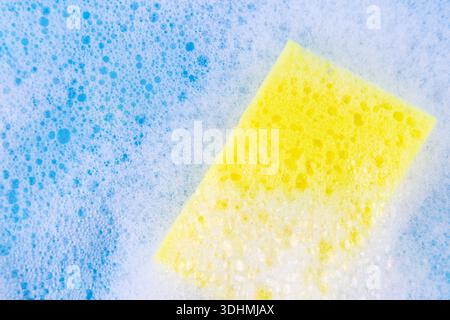 éponge jaune en mousse blanche à bulles pour laver la vaisselle. Gant de toilette recouvert de savon. Corvées domestiques et concept de fournitures. Détergent pour vaisselle sensible. cl Banque D'Images