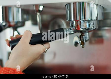 Prise de vue ciblée de la main de la femme dans la manchette orange bloquant la poignée espresso dans la tête du groupe. Banque D'Images