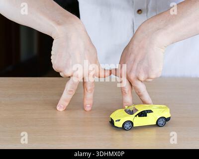 Gros plan des mains avec des doigts imitant des jambes approchant une voiture de sport jaune vif sur une table en bois. Banque D'Images