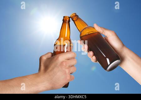 Santé. Hommes serrant des bouteilles de bière contre le ciel bleu, gros plan Banque D'Images