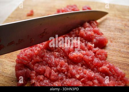 Gros plan sur la texture de viande rouge finement hachée ou hachée avec un couteau sur une planche de bois. Préparation de tartare. Banque D'Images