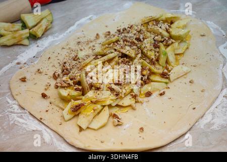 Pâte de levure crue roulée avec une garniture de pomme et de noix sur le dessus. Préparation de tarte tressée sucrée maison. Banque D'Images